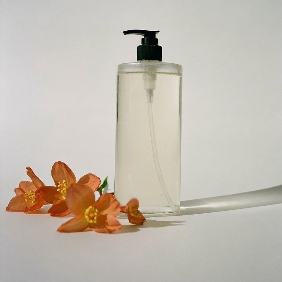 Flacone in vetro trasparente con pompetta dell'Acqua Micellare Zagara accanto a fiori d'arancio