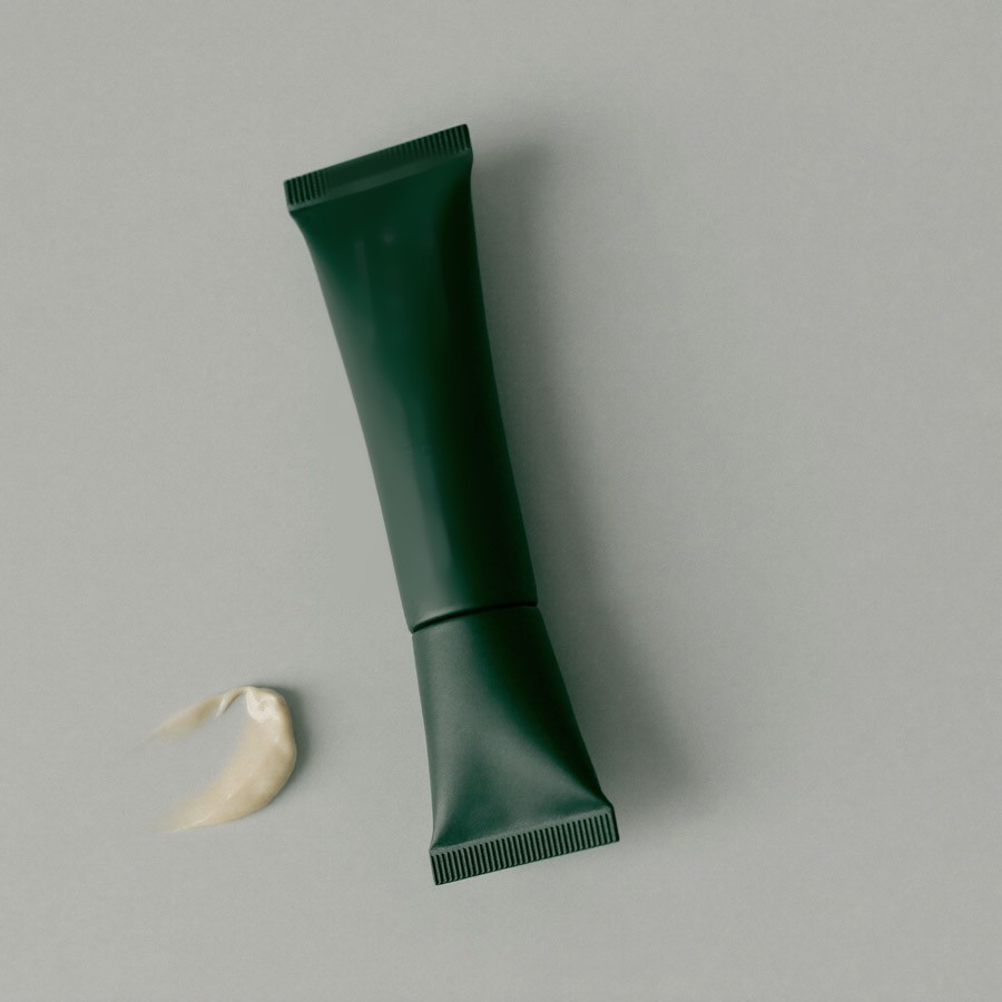 Tubetto in alluminio verde scuro del Contorno Occhi Levigante con una piccola dose di crema accanto