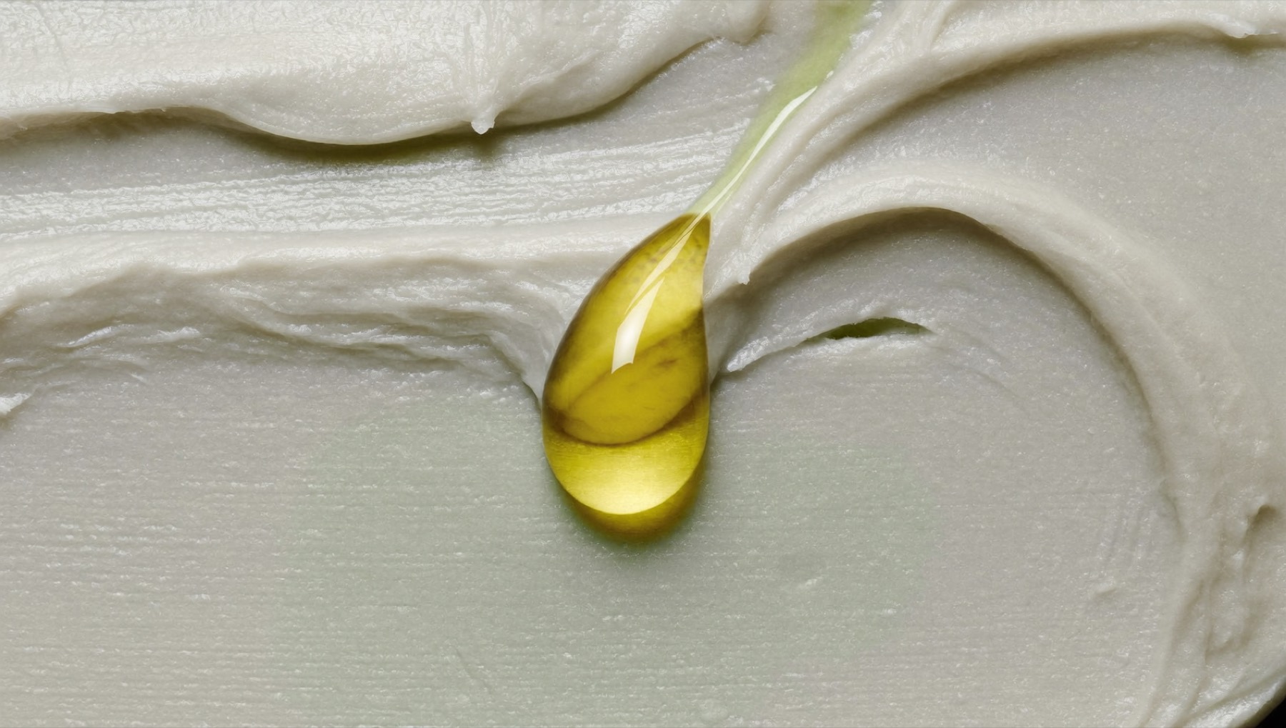 Macro di una texture di crema bianca con una goccia di olio dorato sospesa